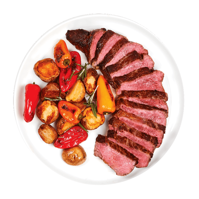 Sliced steak with roasted potatoes and peppers on a white plate