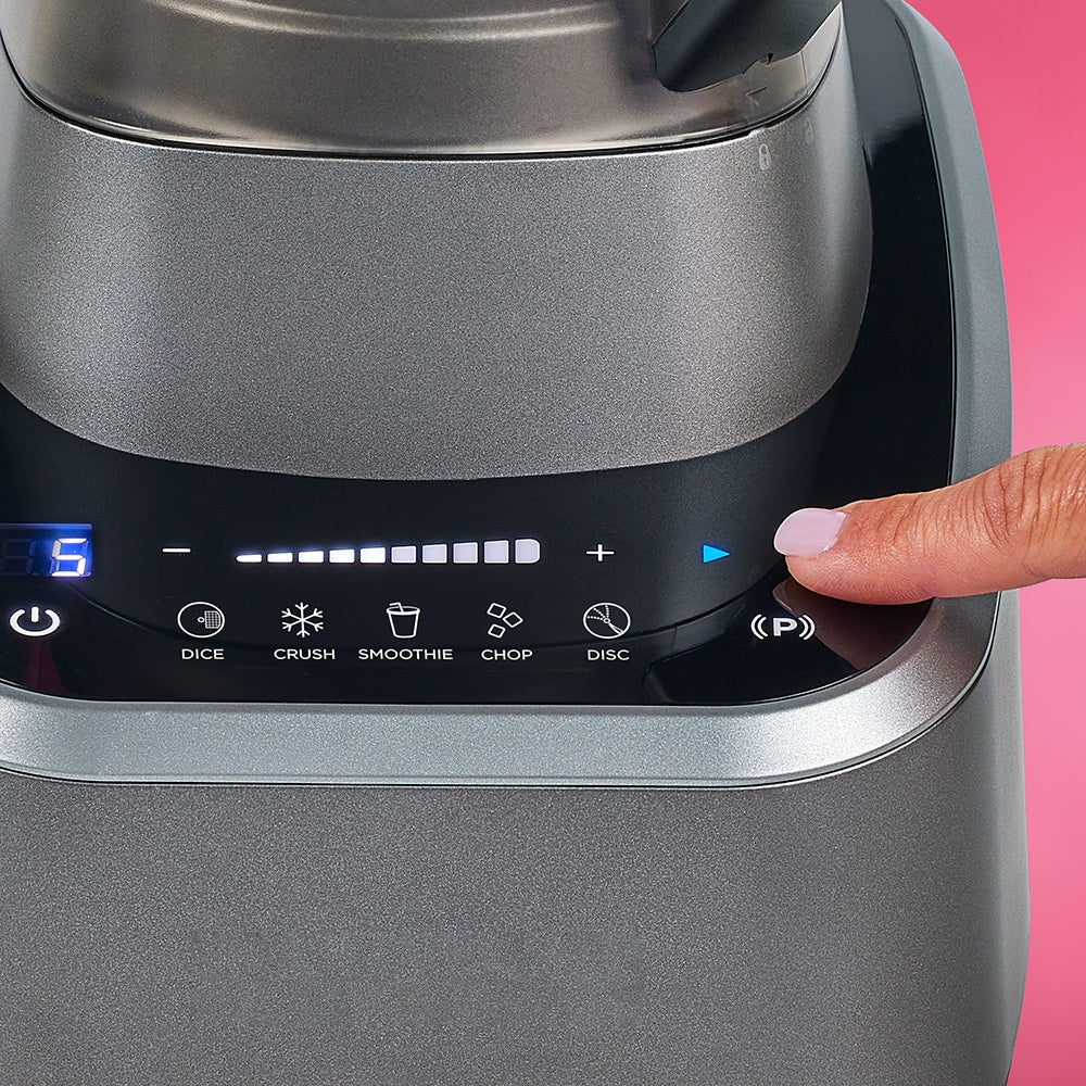 Hand pressing a button on a blender with a pink background
