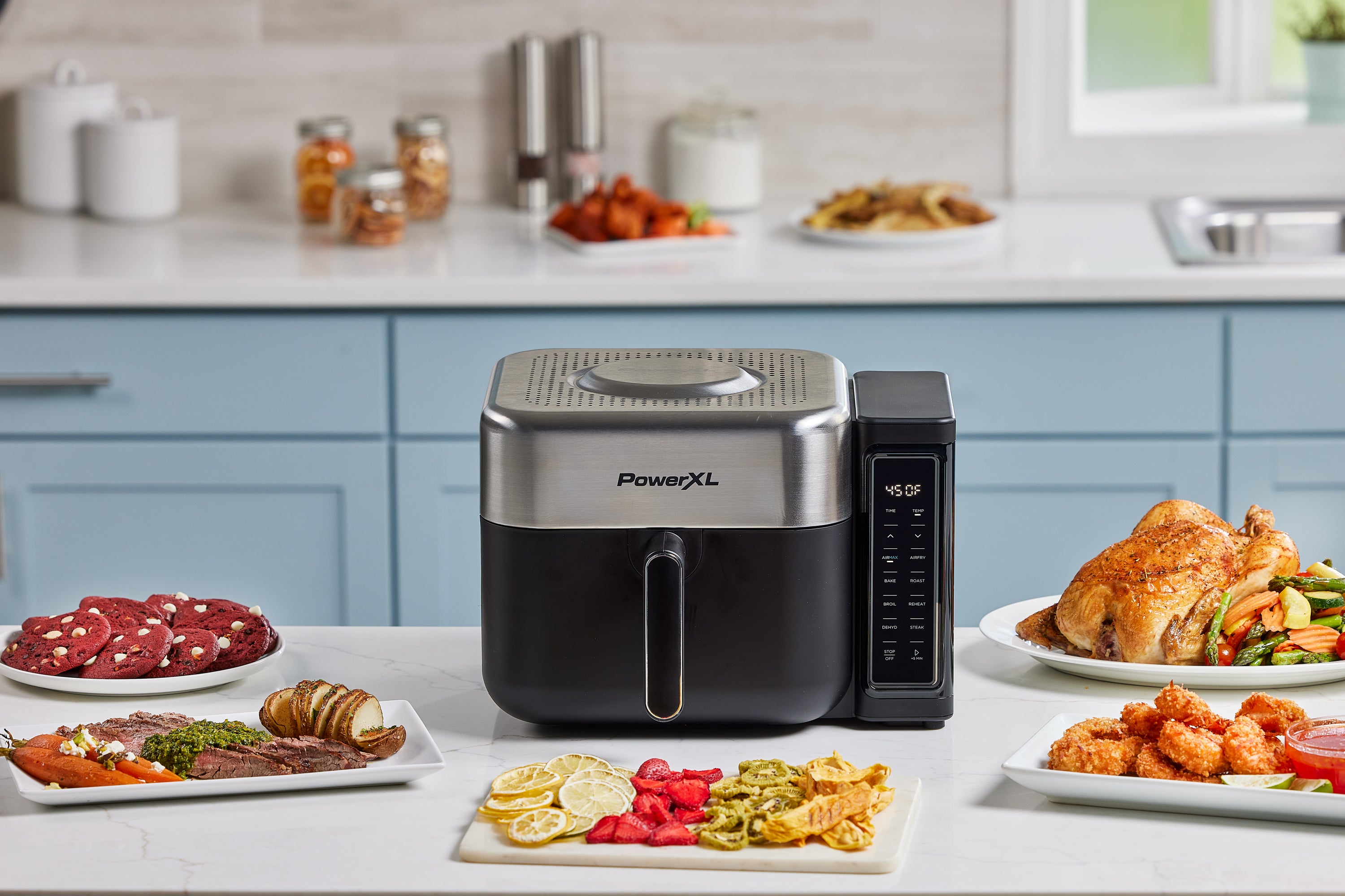 PowerXL air fryer on a kitchen counter with various cooked foods around it.