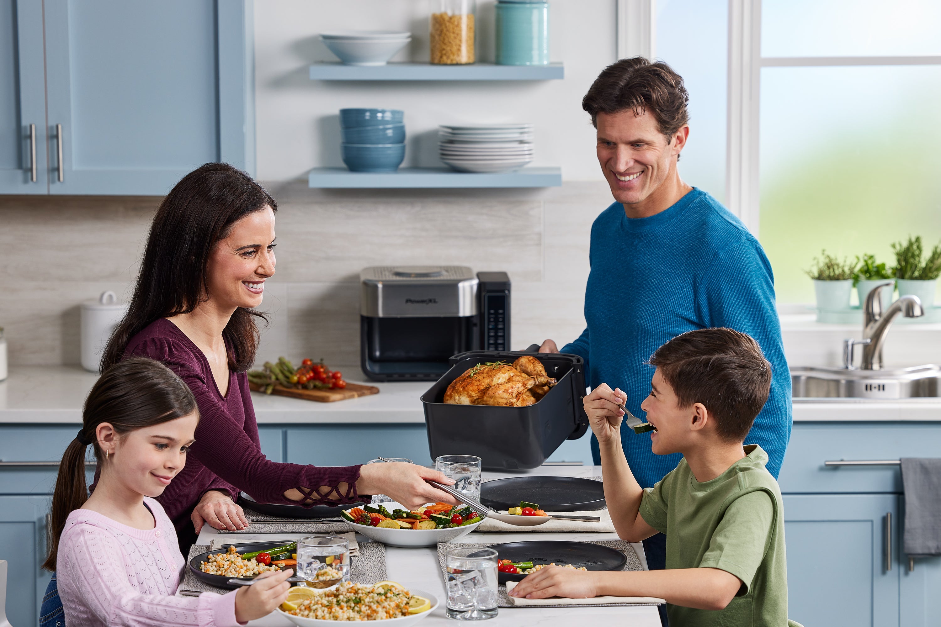 Family of four in a kitchen preparing to eat a meal together.