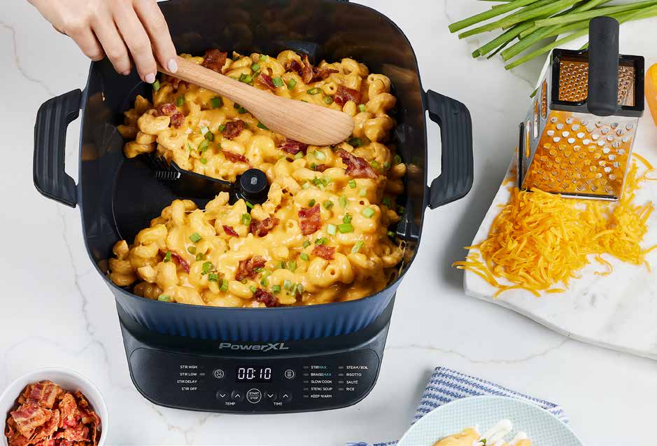 Macaroni and cheese being stirred in a PowerXL Multi-cooker with shredded cheese on the side.