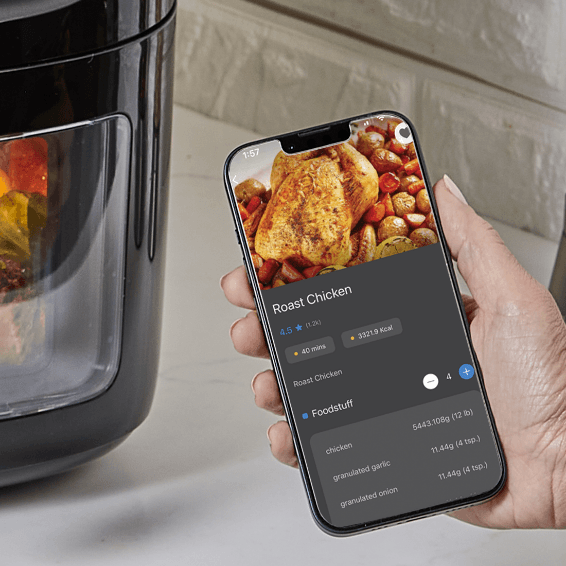 Person holding a smartphone with an app displaying roast chicken recipe next to an air fryer.