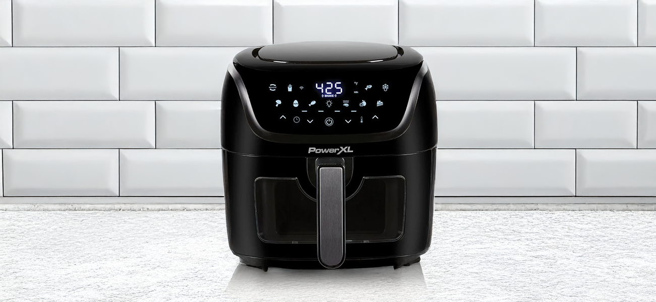Black air fryer on a white tiled floor with a white tiled wall in the background
