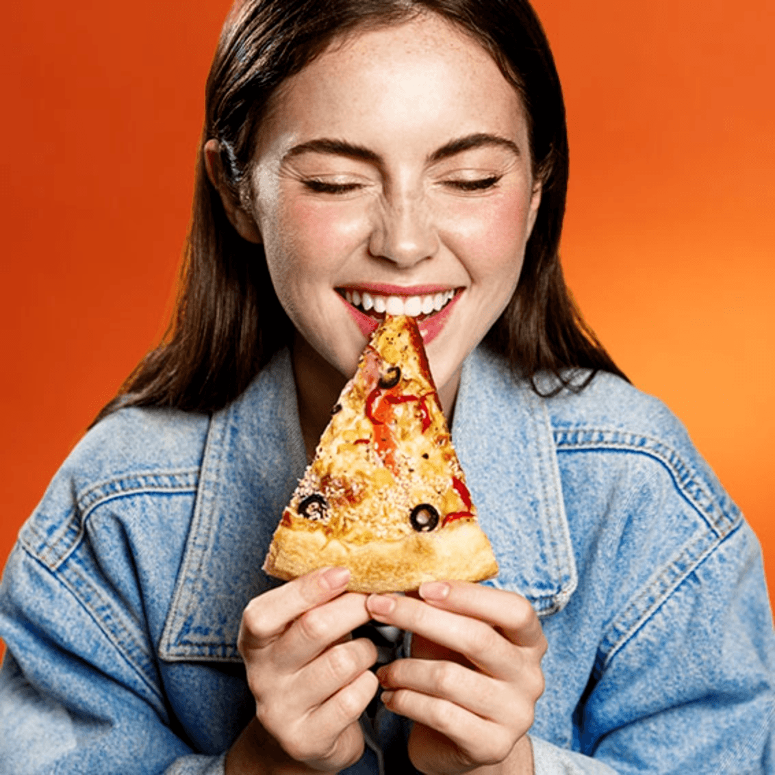 Woman holding a slice of pizza against an orange background