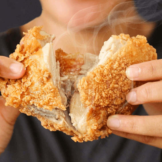 Fried chicken with a crispy exterior held by hands, with steam rising from it.